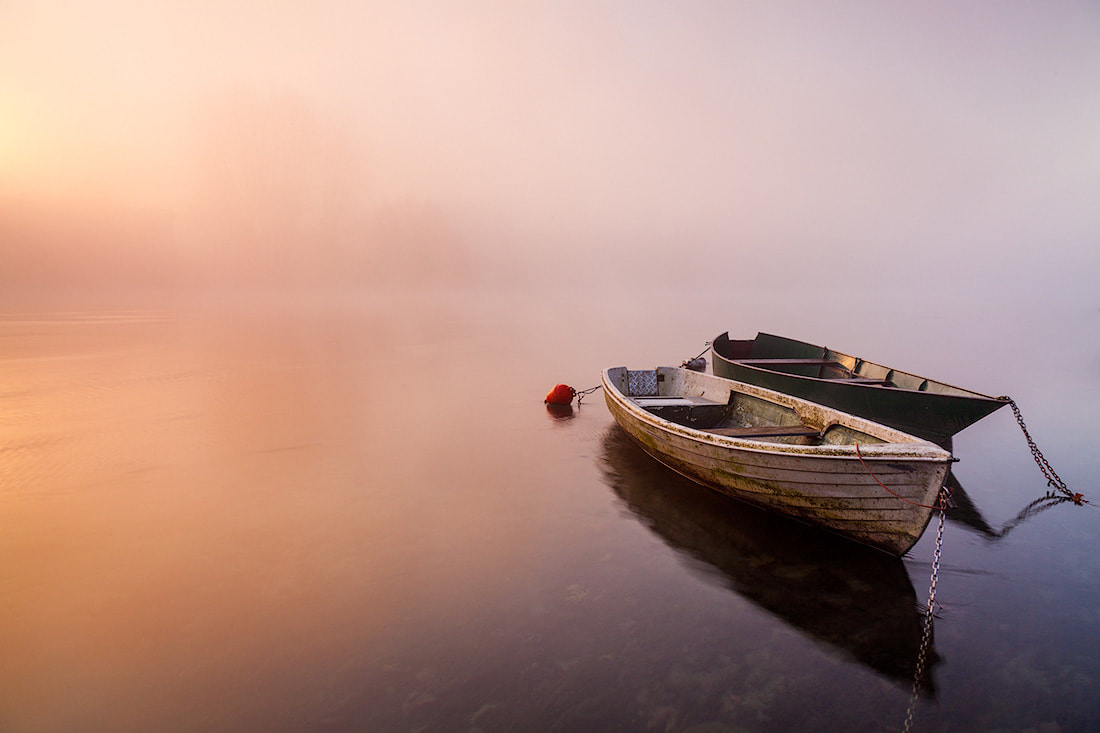 Due barche di legno vicine tra loro nella nebbia all'alba sul fiume Adda a Brivio