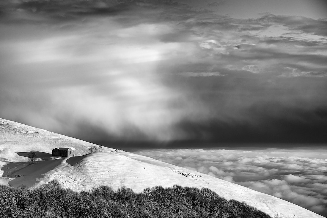Nuvole basse sulla pianura padana e una casetta sul monte Linzone ammantato di neve fresca