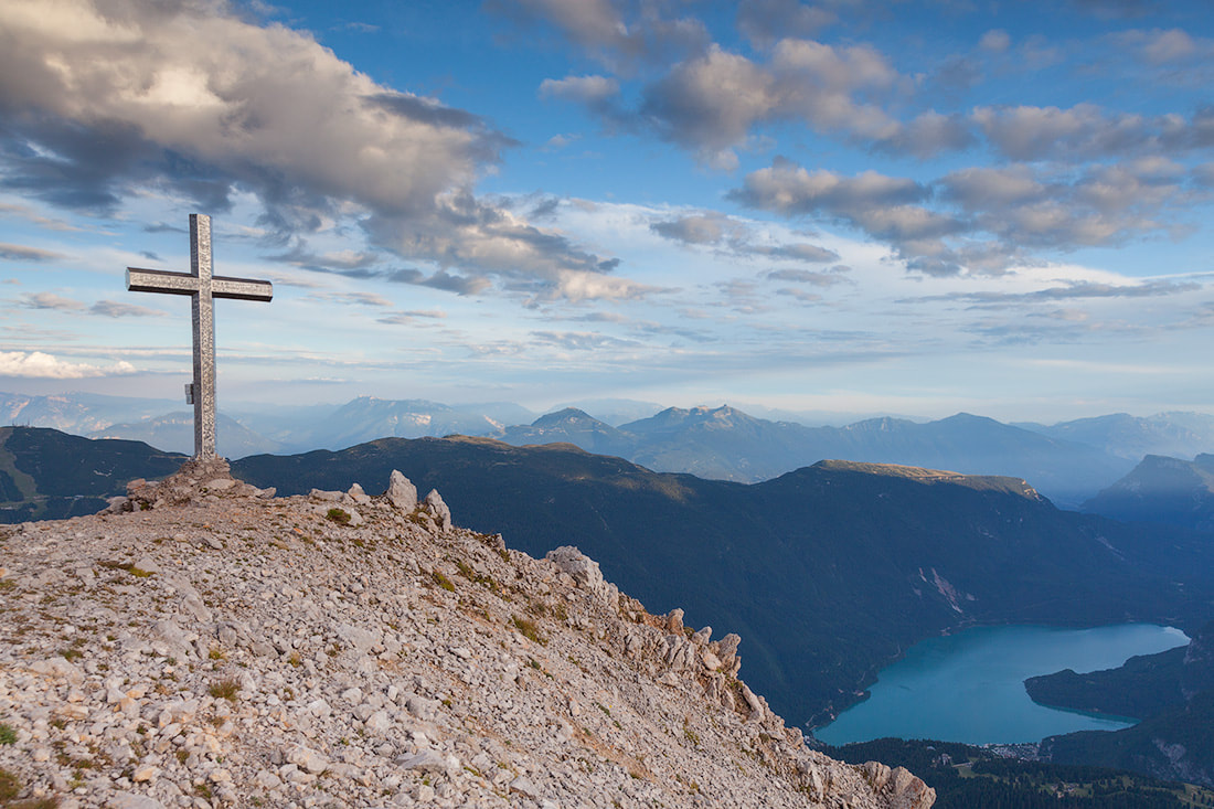Croce sulla vetta del Piz Galin in una giornata di sole. In basso a destra si vede il lago di Molveno